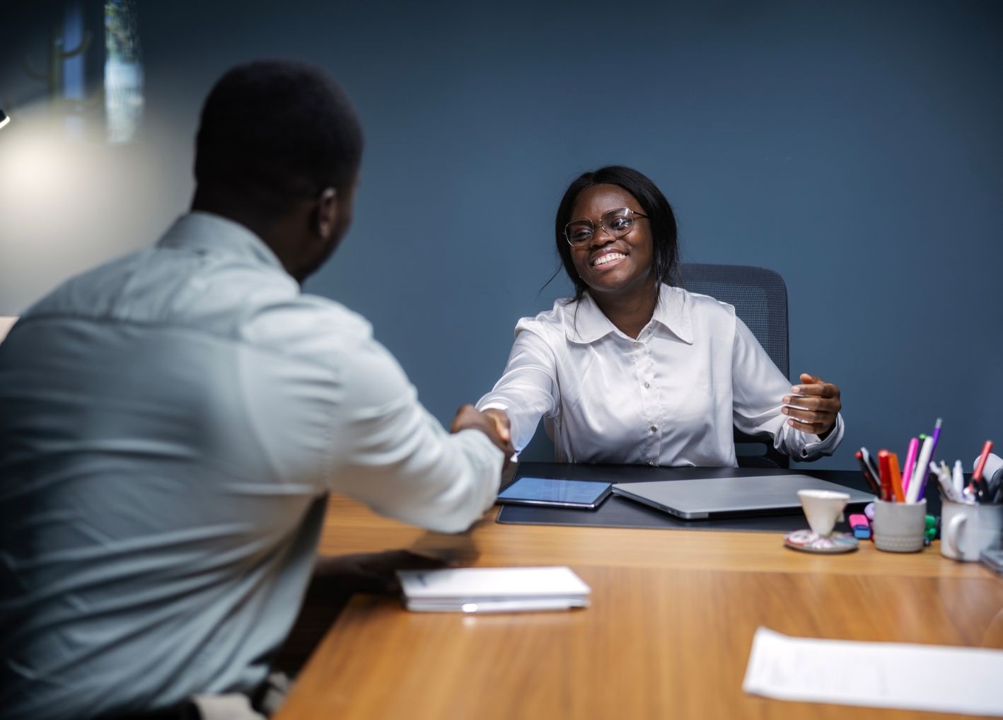 Two individuals seated at a table shaking hands in an office setting