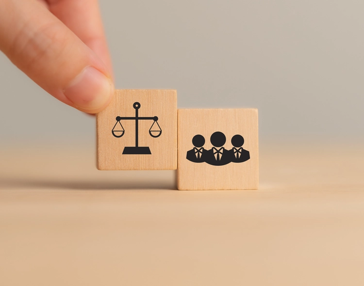 Hand holding wooden block depicting employees and justice scales.