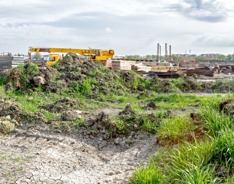 Grassy construction zone with construction vehicles and smokestacks in background