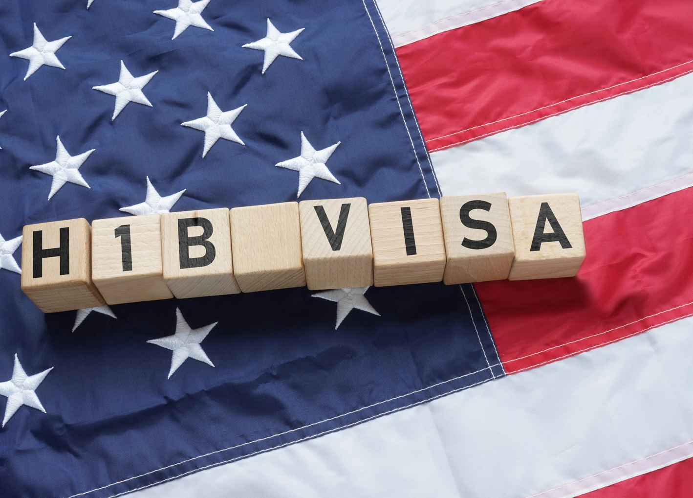 H-1B visa spelled out in wooden blocks over an American flag.
